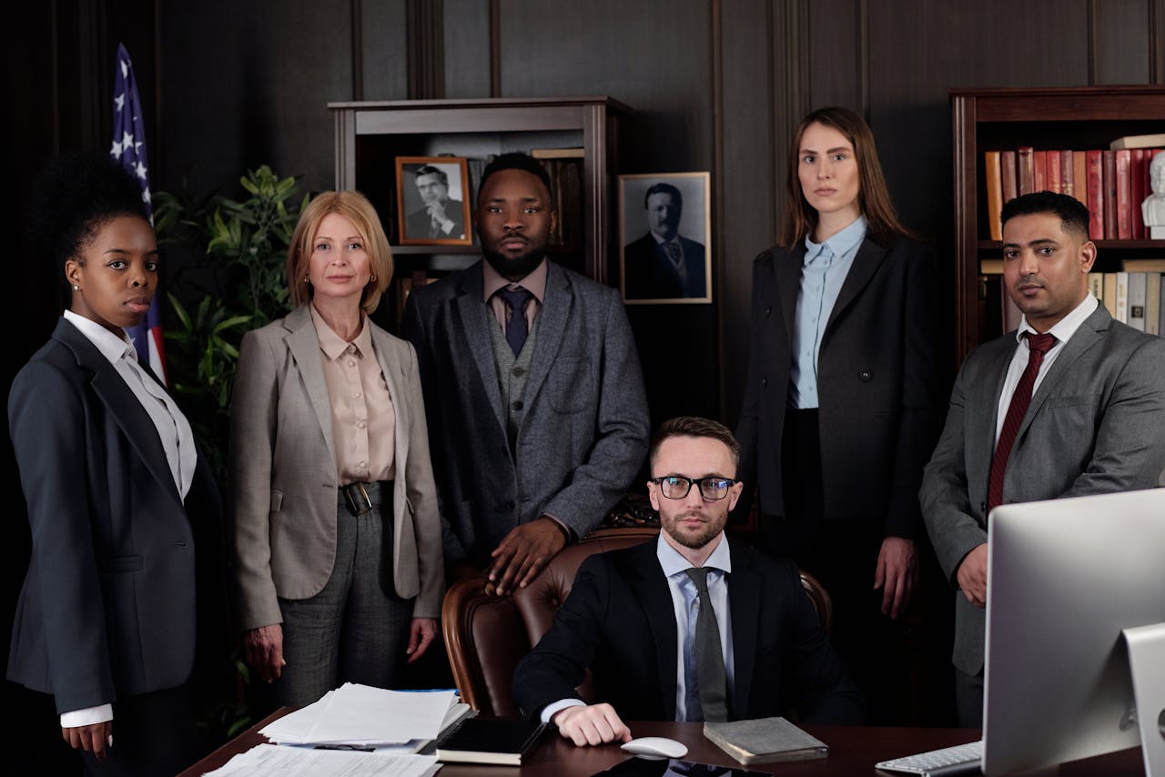 gallery-5 A diverse group of business professionals posing in an office, showcasing teamwork and leadership.