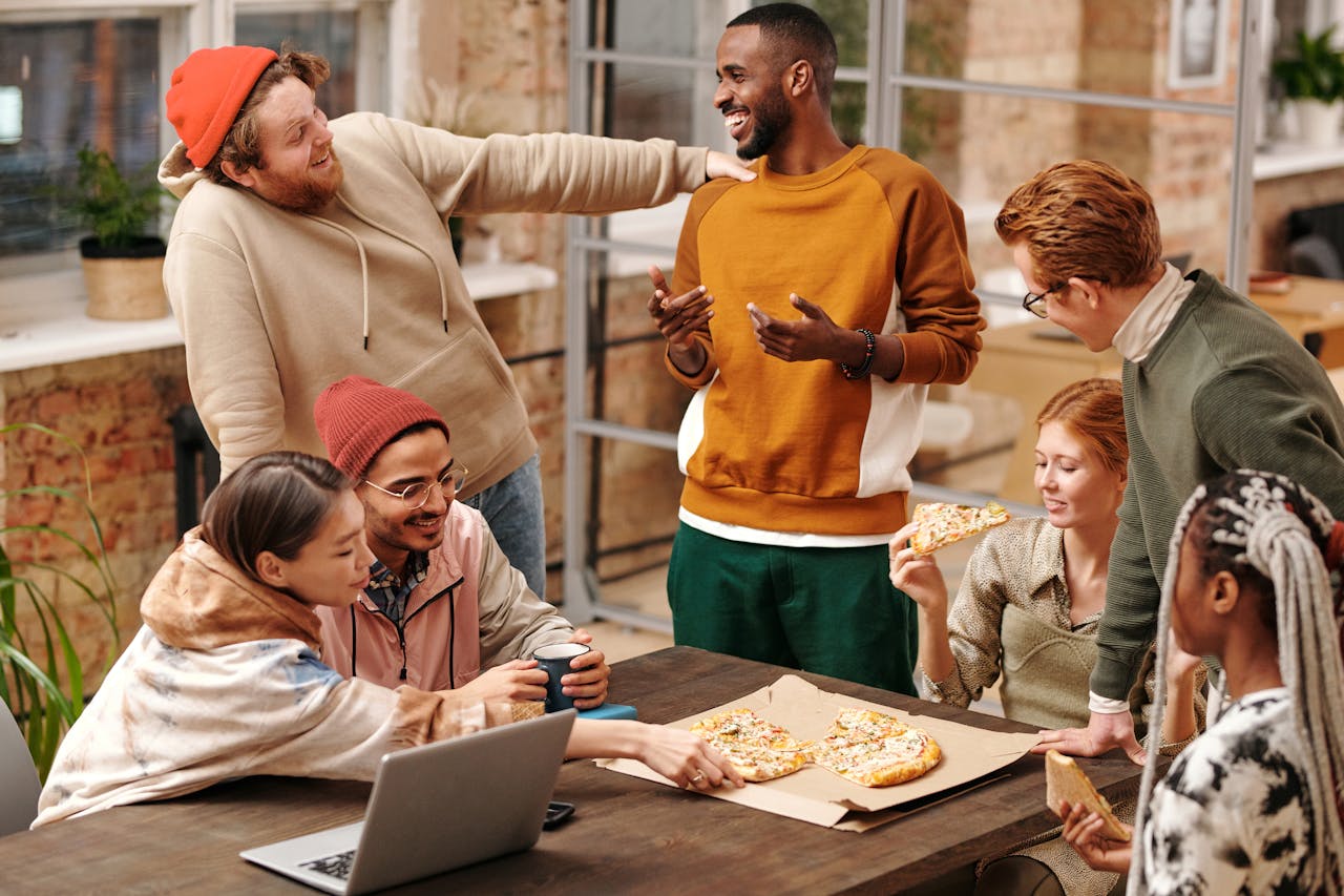 why-choose-us A group of diverse friends laughing and enjoying pizza together indoors.