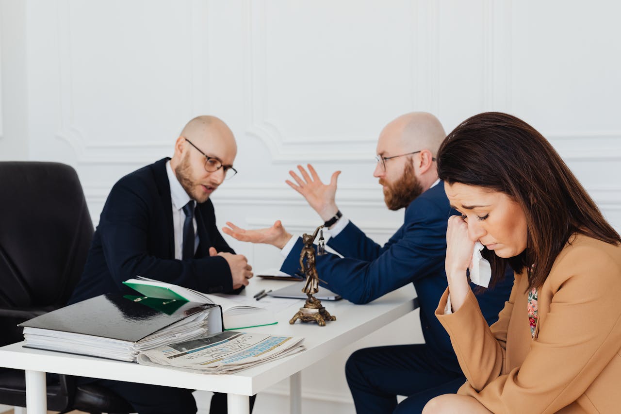 gallery-6 A woman appears distressed while two lawyers converse in an office.